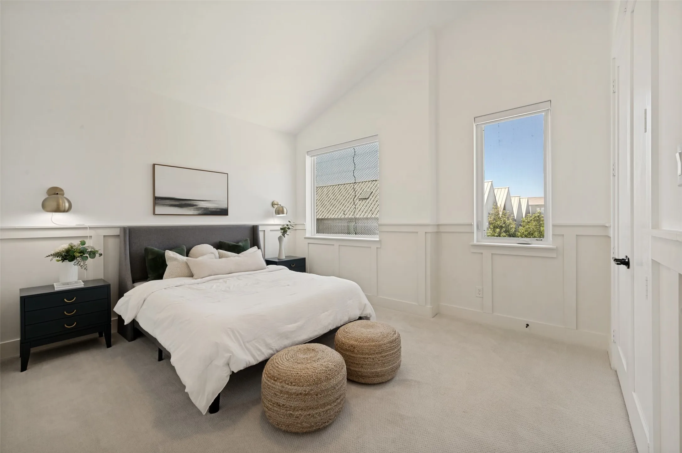 Vaulted ceiling, two windows, wall paneling, sconce lighting, and a paneled door