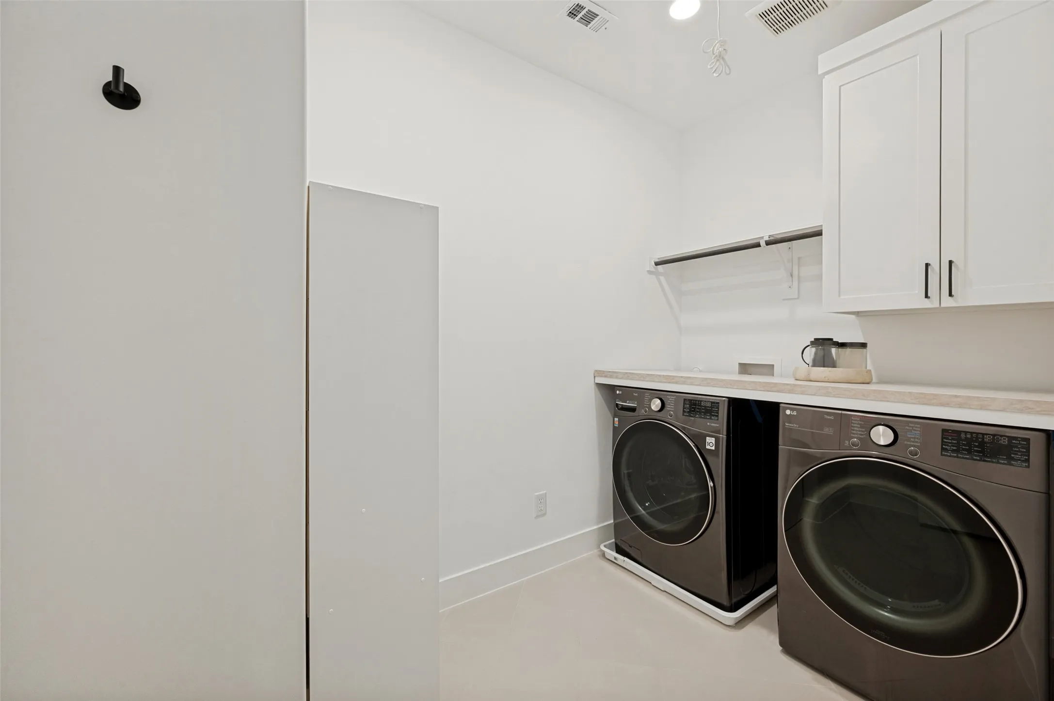 White shaker-style cabinetry with black hardware, light-toned countertop, and an upper shelving unit