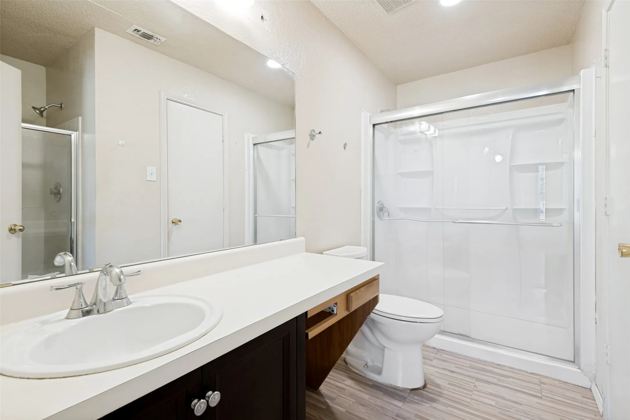 White countertop vanity with an oval sink, chrome faucet, dark wood-finish cabinetry, and a shower with a sliding glass door