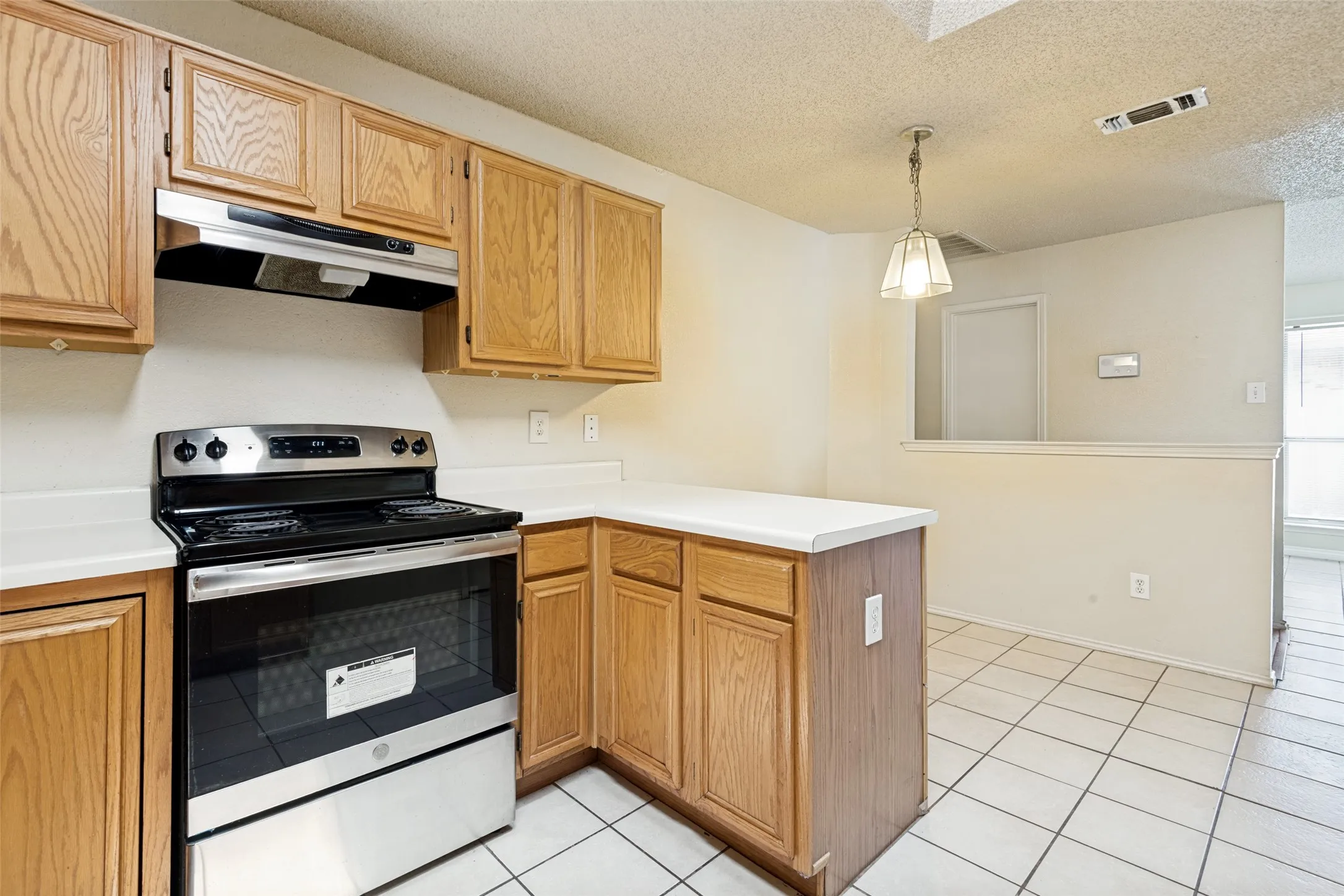 Spacious kitchen featuring wood-finish cabinetry, stainless steel electric range with convection oven, white tile countertops, and ceramic tile flooring