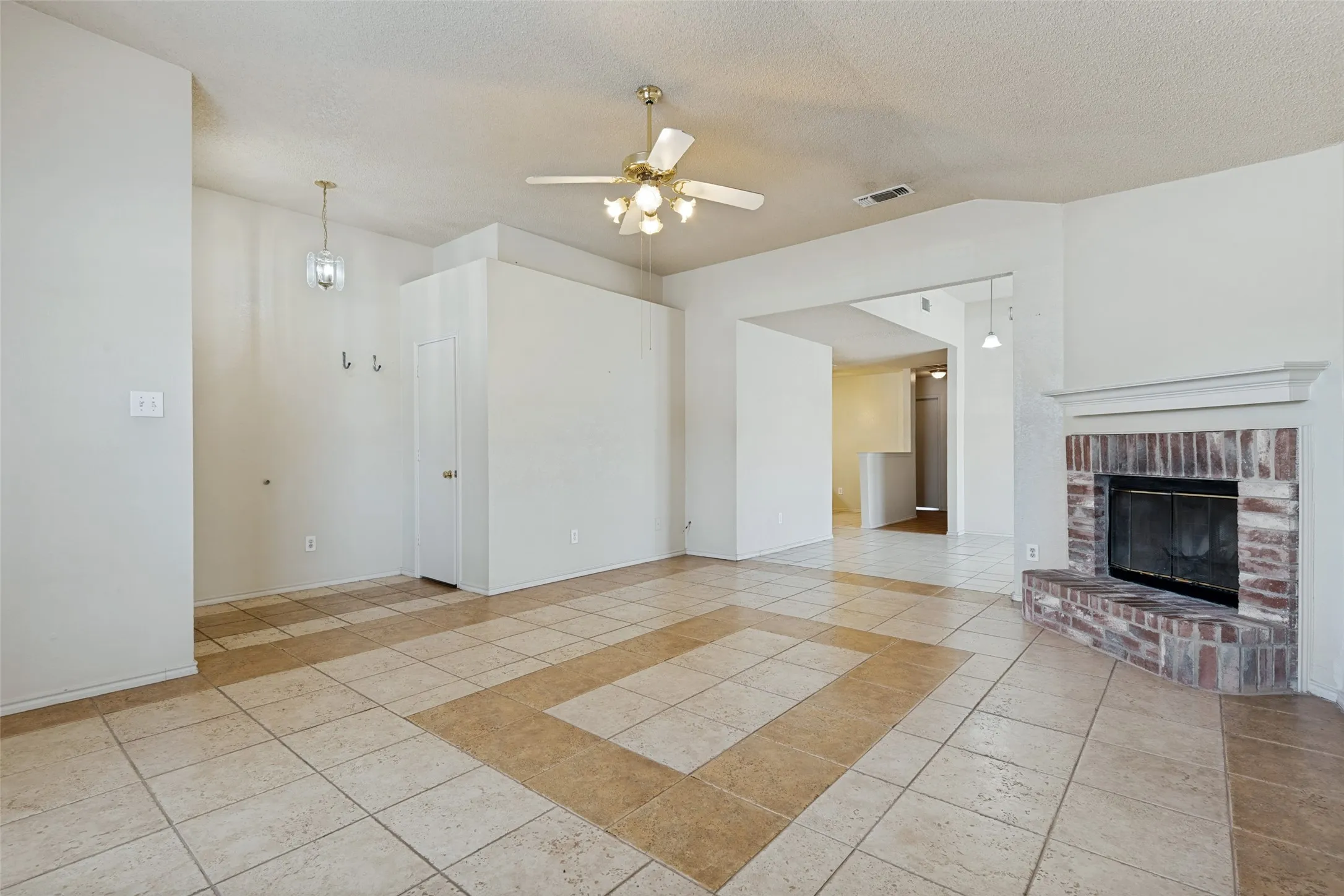 Tile flooring with an accent border, a brick fireplace with a mantel, a ceiling fan, a built-in storage closet, and a wall-mounted light fixture