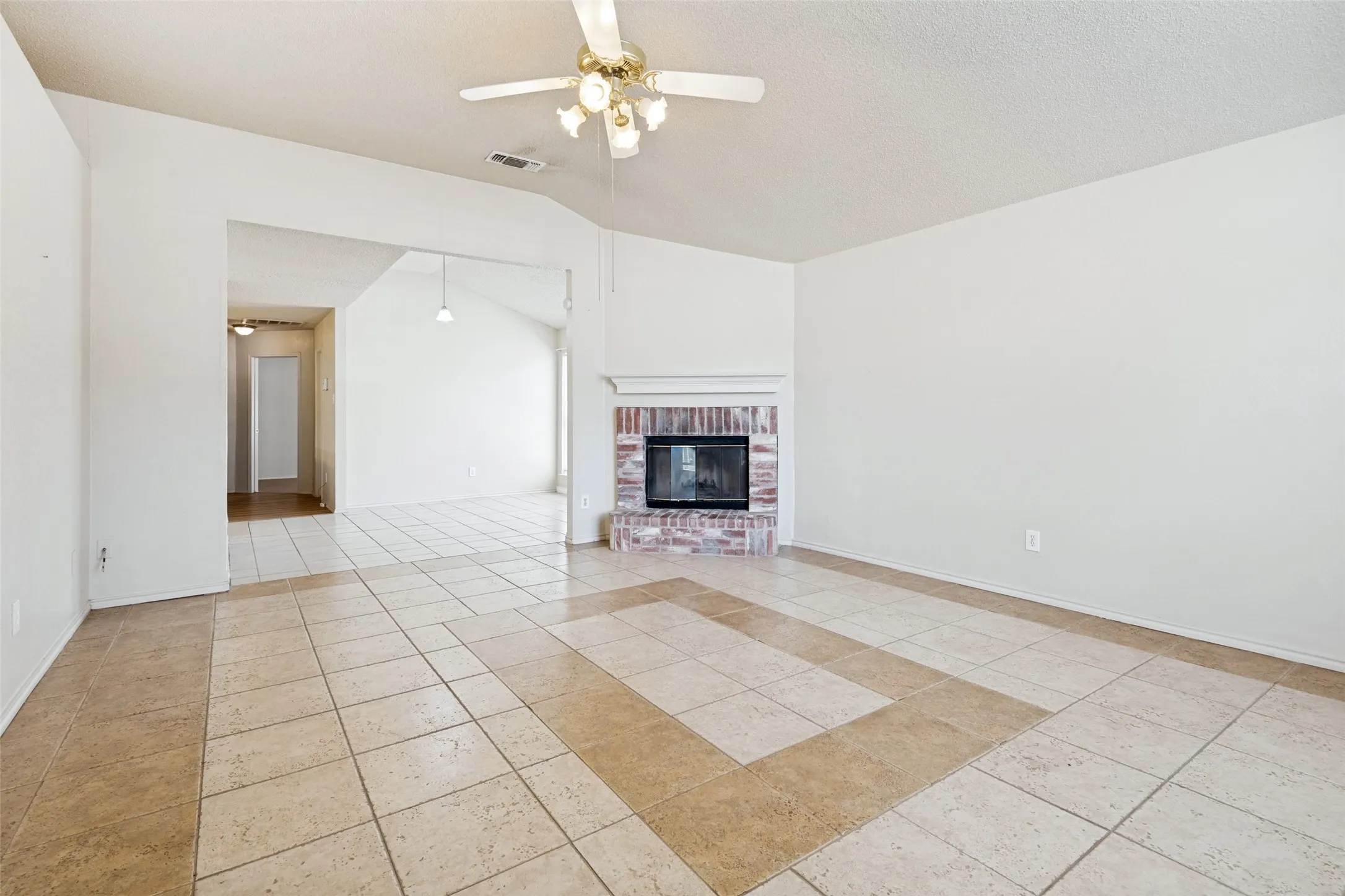 Vaulted ceiling with a ceiling fan, brick fireplace, and tile flooring with a decorative inlay