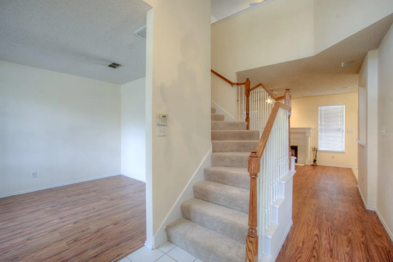 Two-story ceiling, wood-finish flooring, carpeted staircase, fireplace with white mantel, and white interior walls