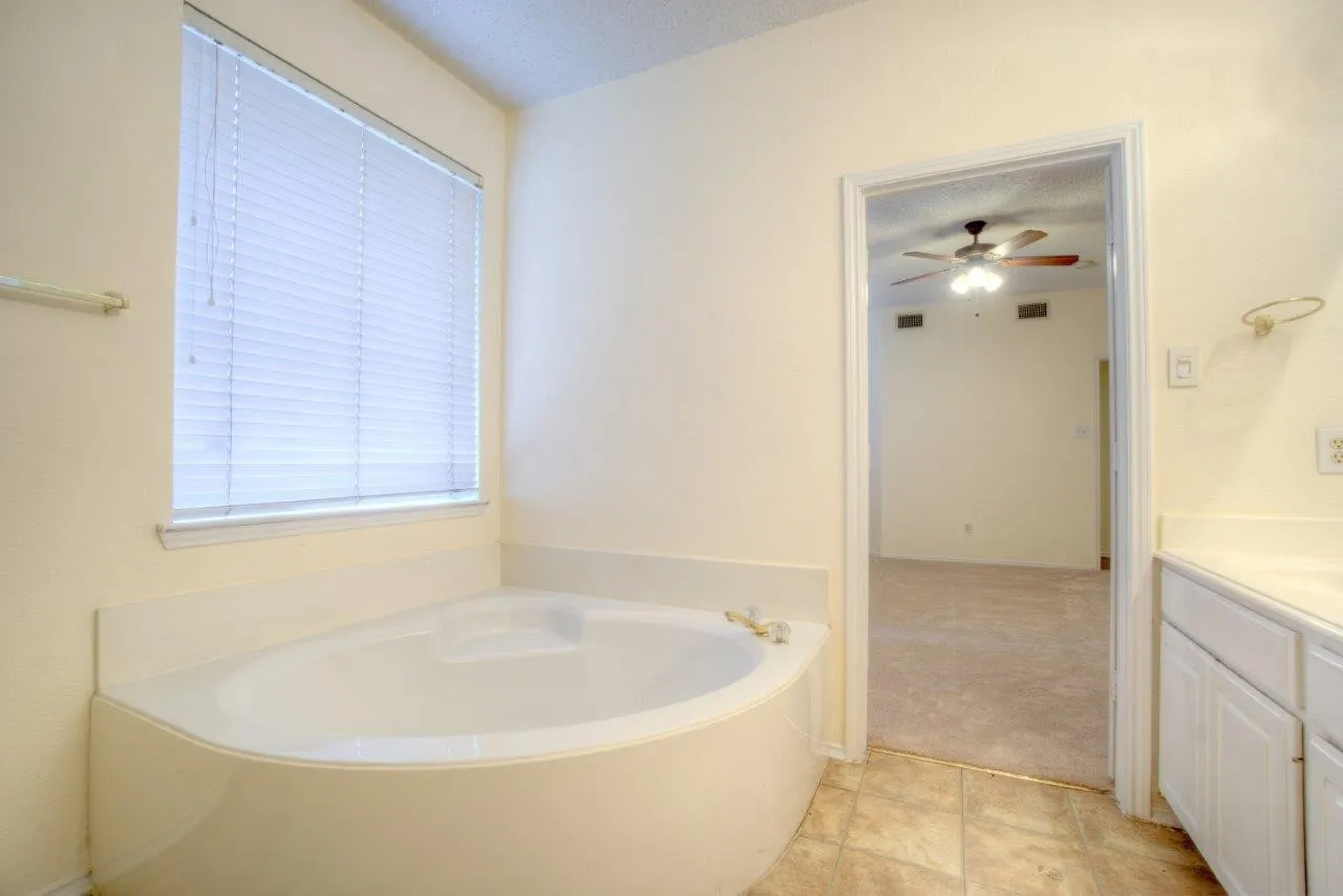 Bathroom featuring a corner soaking tub, window with blinds, tile flooring, and vanity with built-in cabinetry