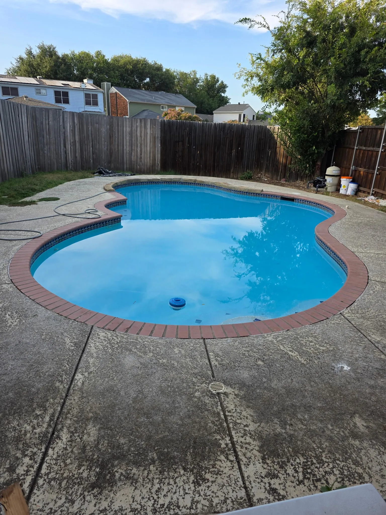 Freeform swimming pool with a brick coping, surrounded by a concrete patio and wood fencing