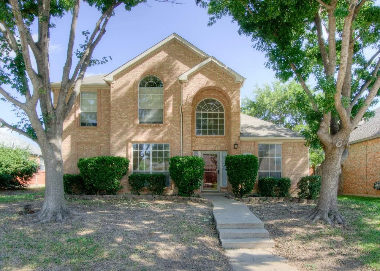 Brick exterior, arched windows, gabled roofline, mature trees, and a concrete walkway with steps
