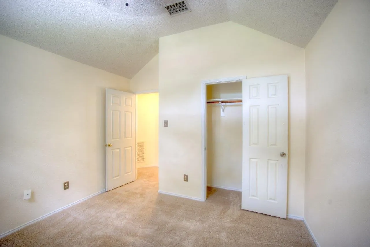 Vaulted ceiling with textured finish, carpeted flooring, and a built-in closet with shelving and hanging rod