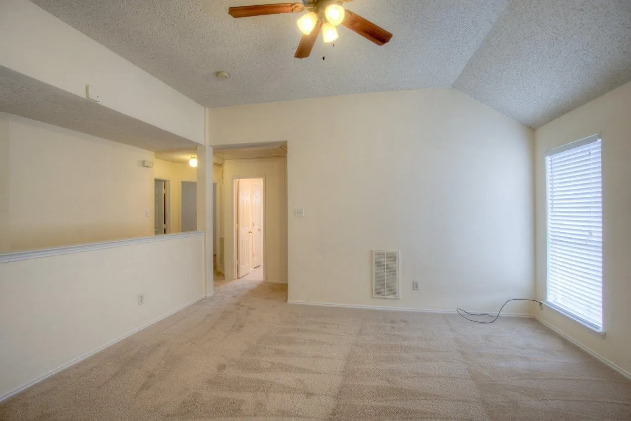 Vaulted ceiling with a ceiling fan, carpeted flooring, and a large window with blinds