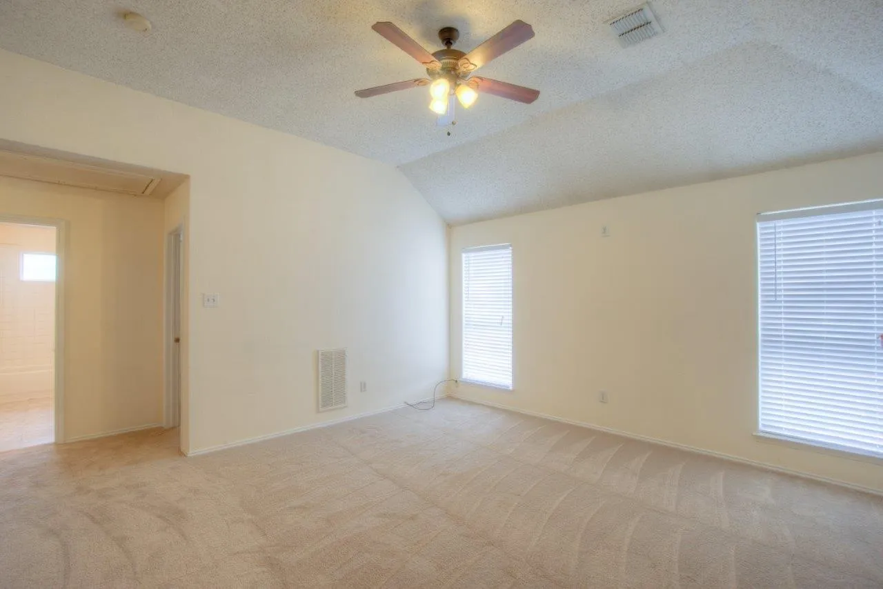 Vaulted ceiling featuring a ceiling fan, carpeted flooring, and multiple windows with blinds