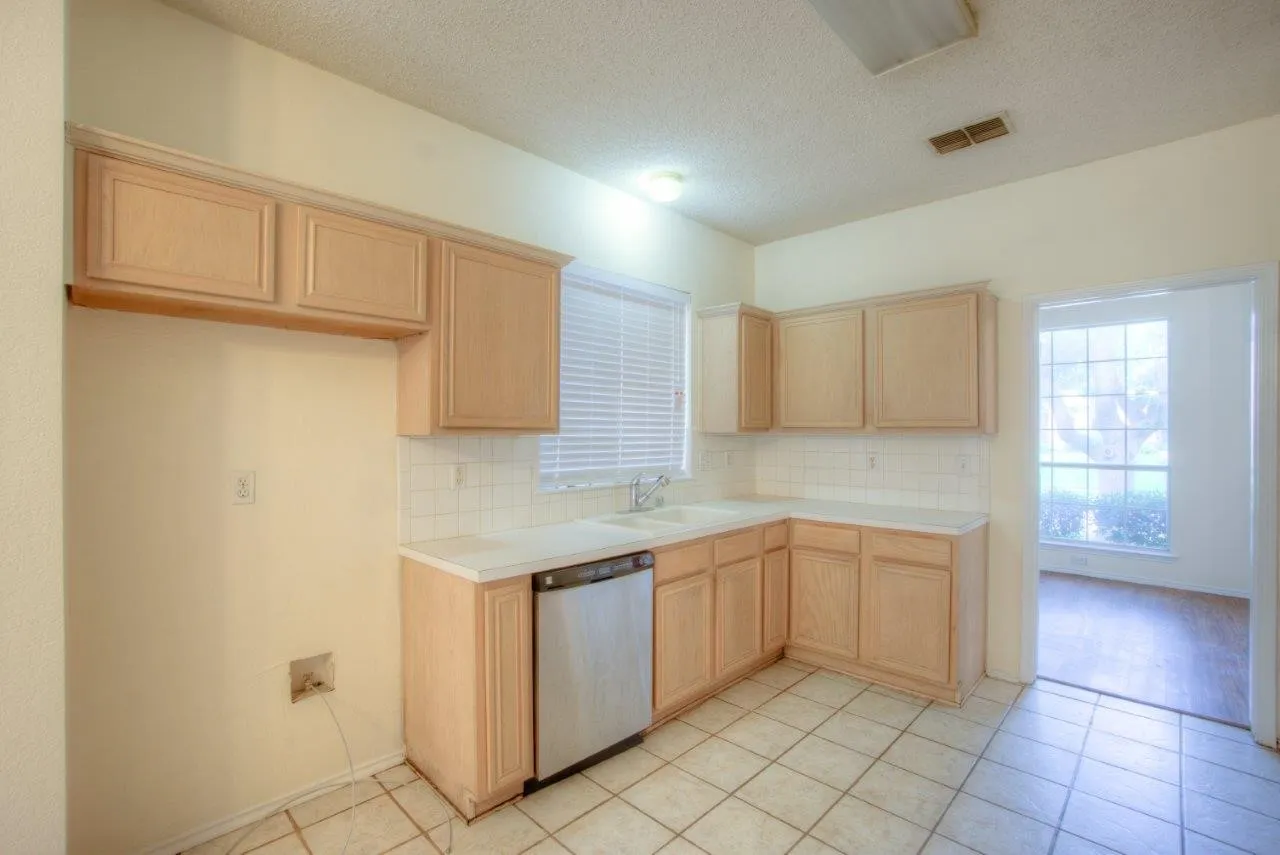 Kitchen featuring wood-finish cabinetry, white countertops, a tile backsplash, and a built-in dishwasher