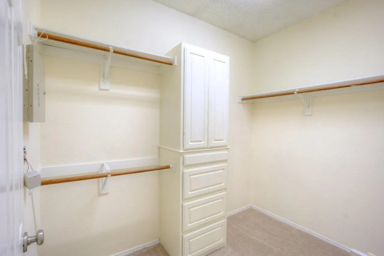 Built-in cabinetry with multiple drawers, two hanging rods, and carpet flooring