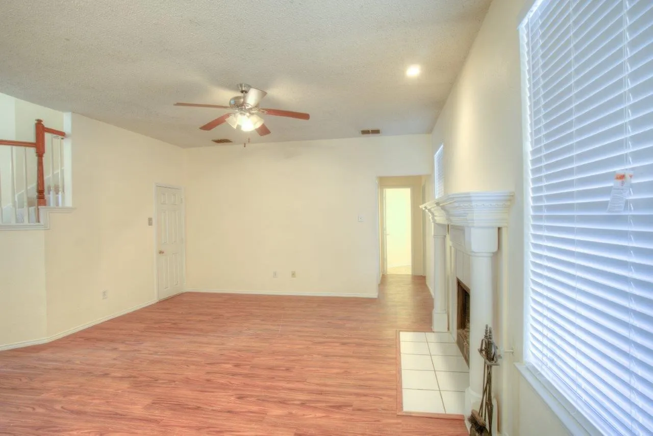 Expansive living area featuring wood-finish flooring, a decorative fireplace with a tile hearth, and a ceiling fan with integrated lighting
