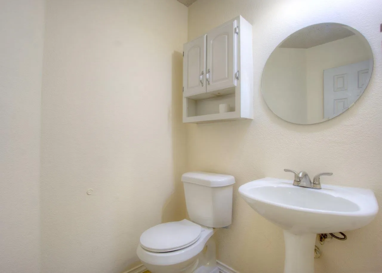 Pedestal sink with chrome faucet, toilet, wall-mounted storage cabinet, and circular mirror