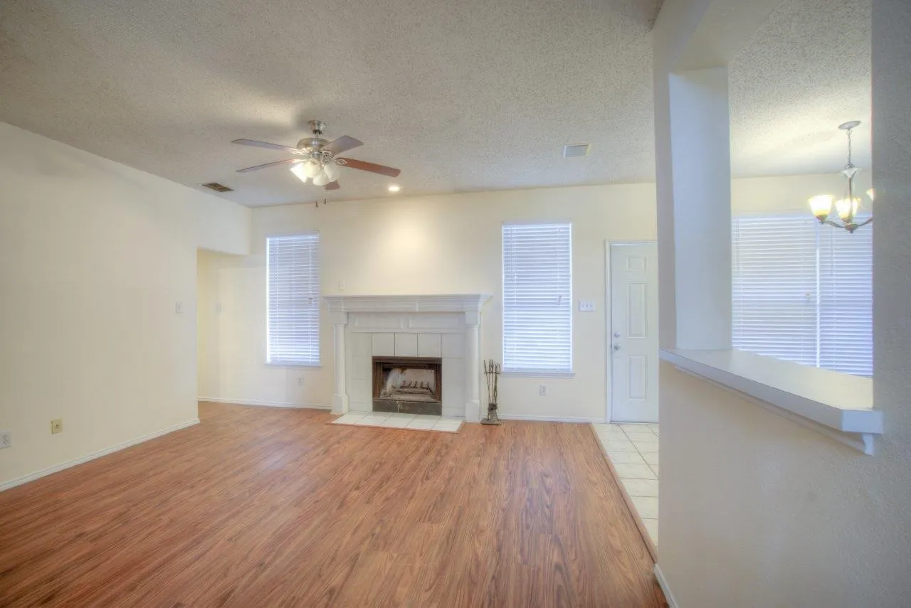 Wood-finish flooring, white tile fireplace surround, ceiling fan, recessed lighting, and a partial wall with a countertop