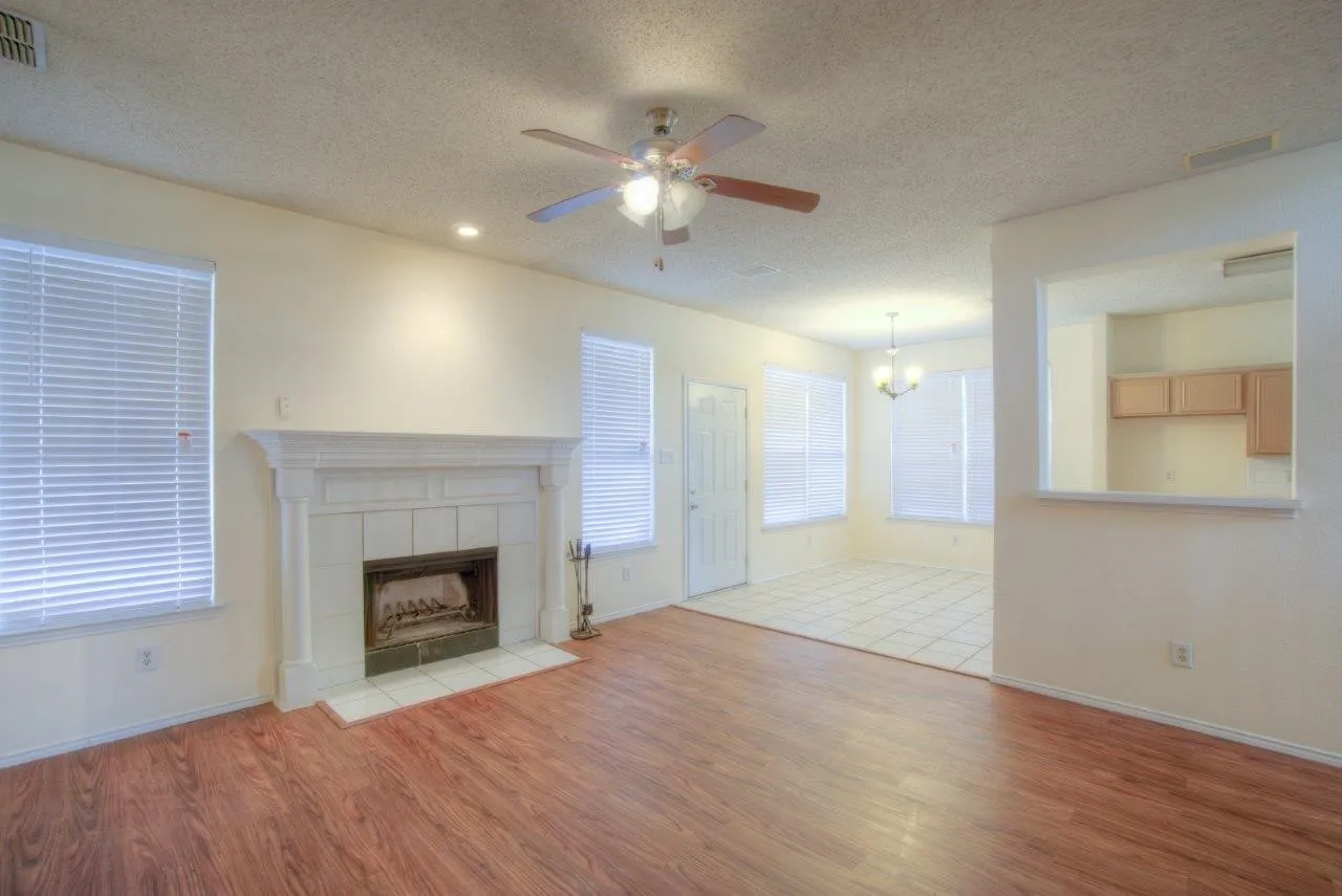 Wood-finish flooring, white tile fireplace surround with decorative mantel, recessed lighting, ceiling fan with light fixture, and a pass-through window to the kitchen