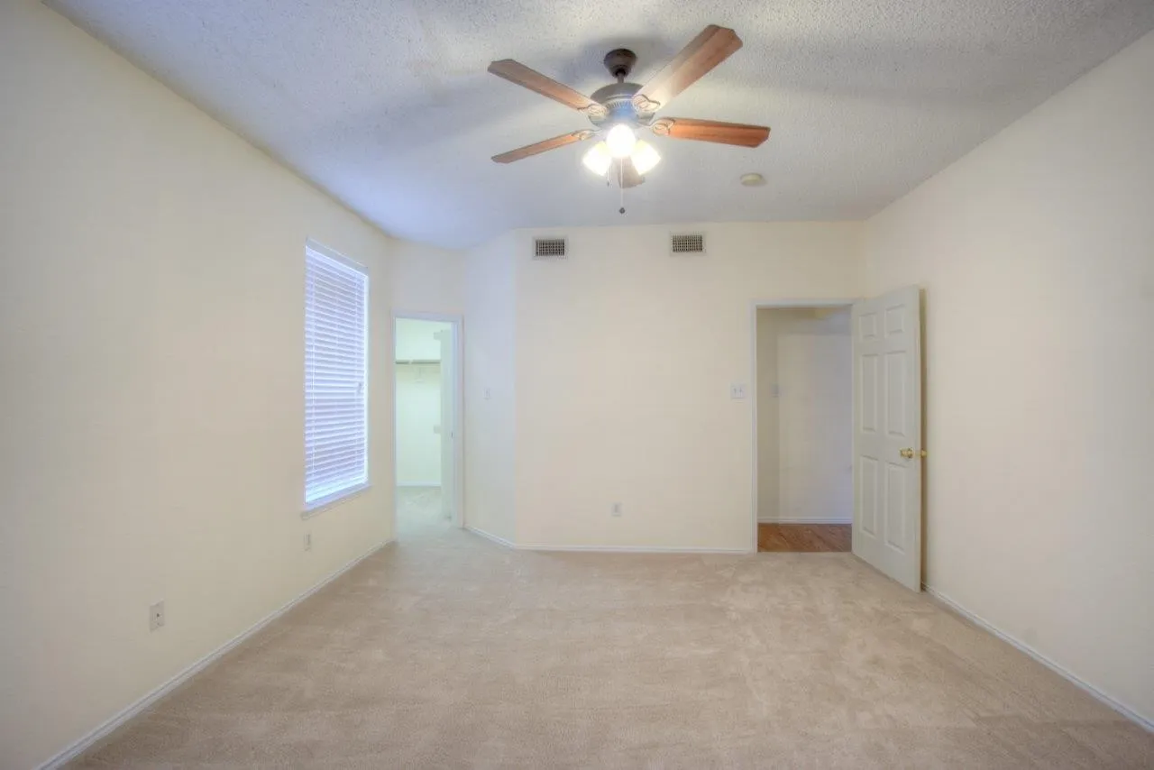 Textured ceiling with a ceiling fan light fixture, neutral carpet flooring, and a window with blinds
