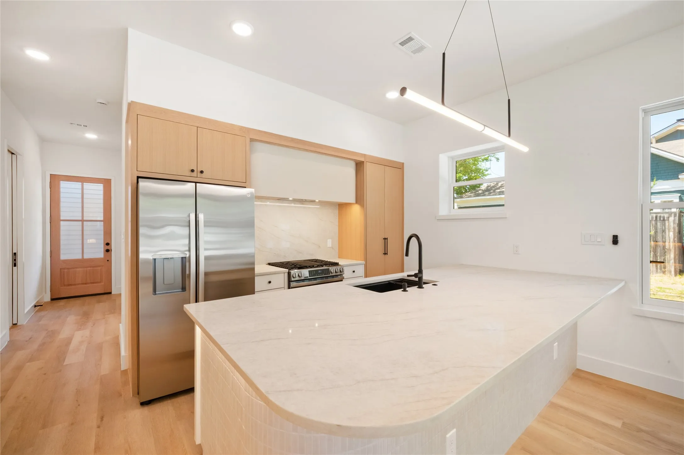 Modern kitchen featuring an expansive island and stainless steel appliances. Hallway to downstairs bedroom and bathroom.