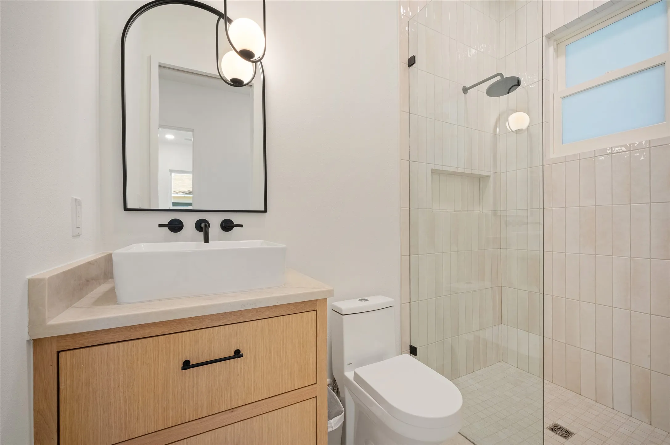 Modern bathroom featuring a wood-finish vanity with a vessel sink, matte black fixtures, and a frameless glass shower enclosure with vertical tile