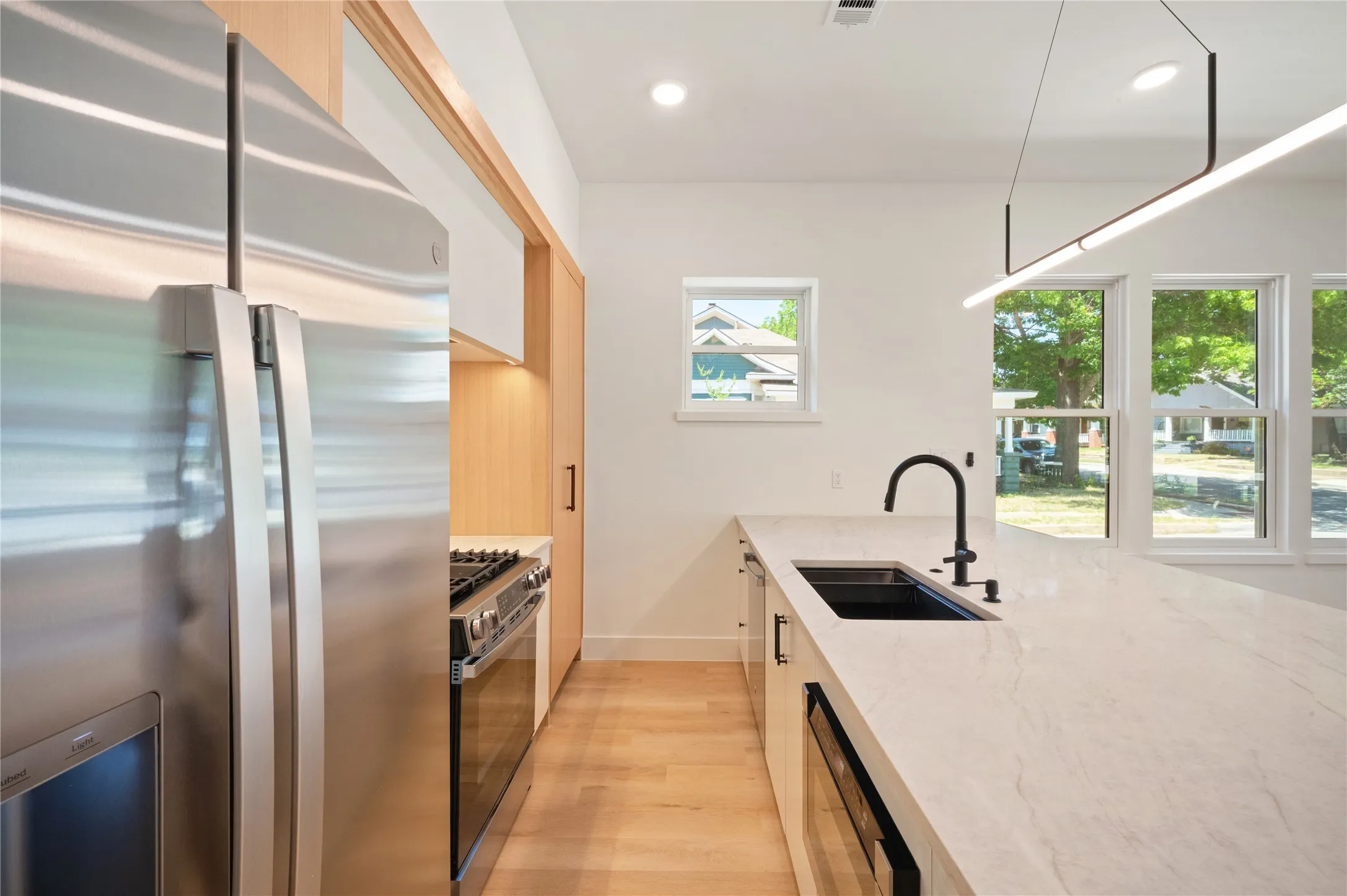 Built in gas range, drawer style microwave, wood-finish flooring, under mount sink with matte black faucet, and white countertops