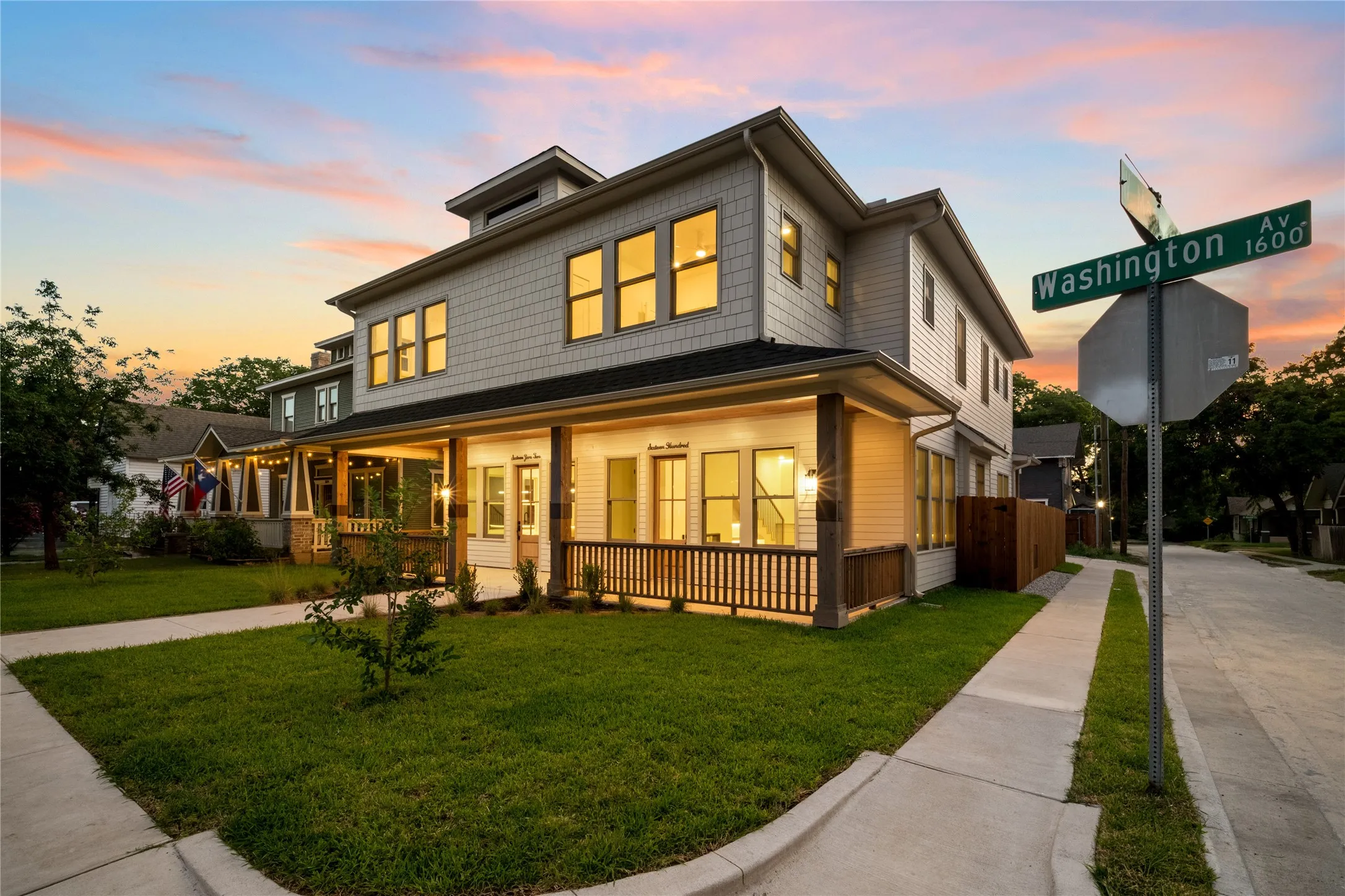 Two-story residence featuring a shingle siding and white paneling exterior, a covered front porch with wood railings, a manicured lawn, and a corner lot location