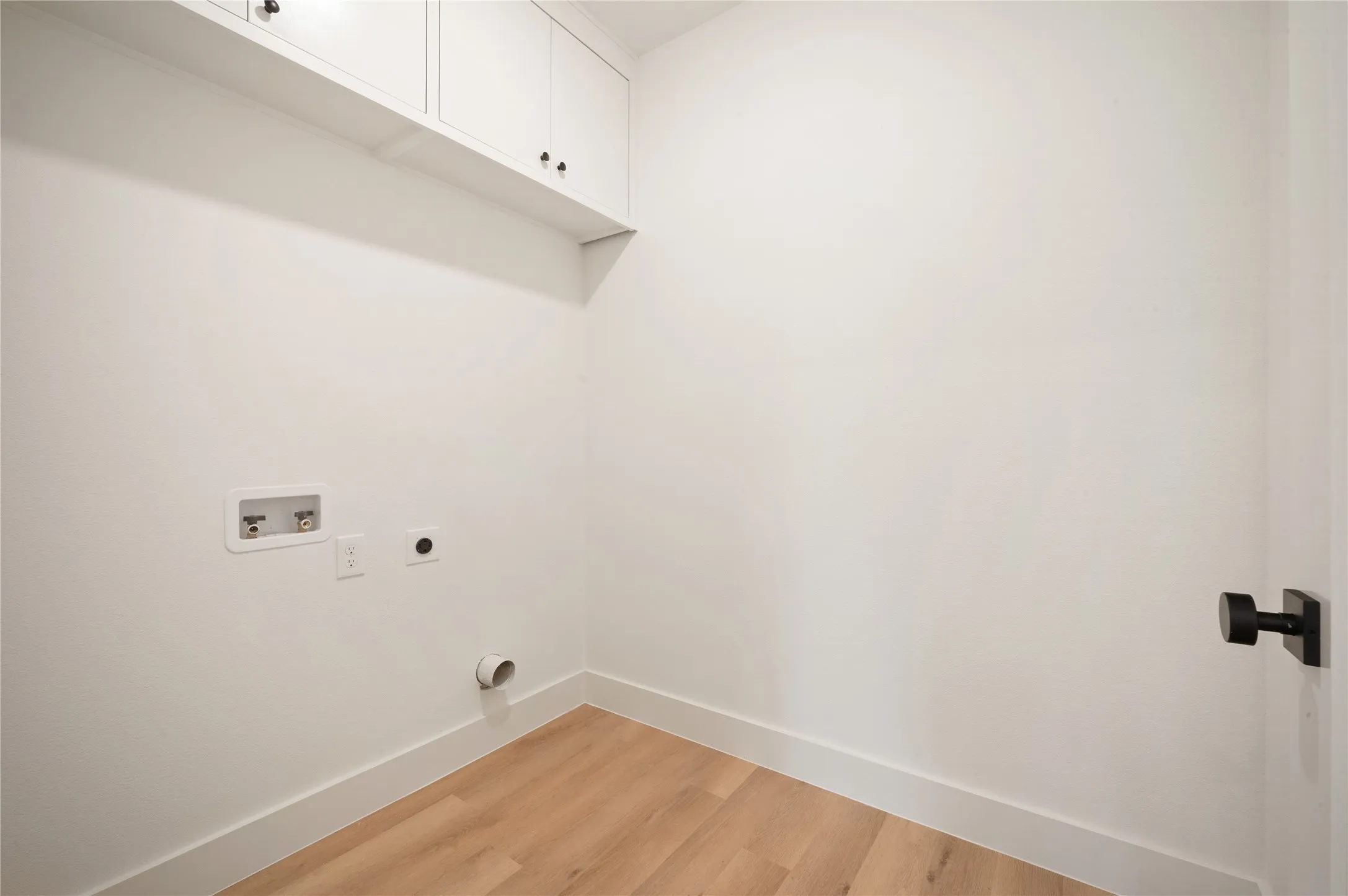 Upstairs utility room with Built-in white cabinetry and matte black hardware, wood-finish flooring.