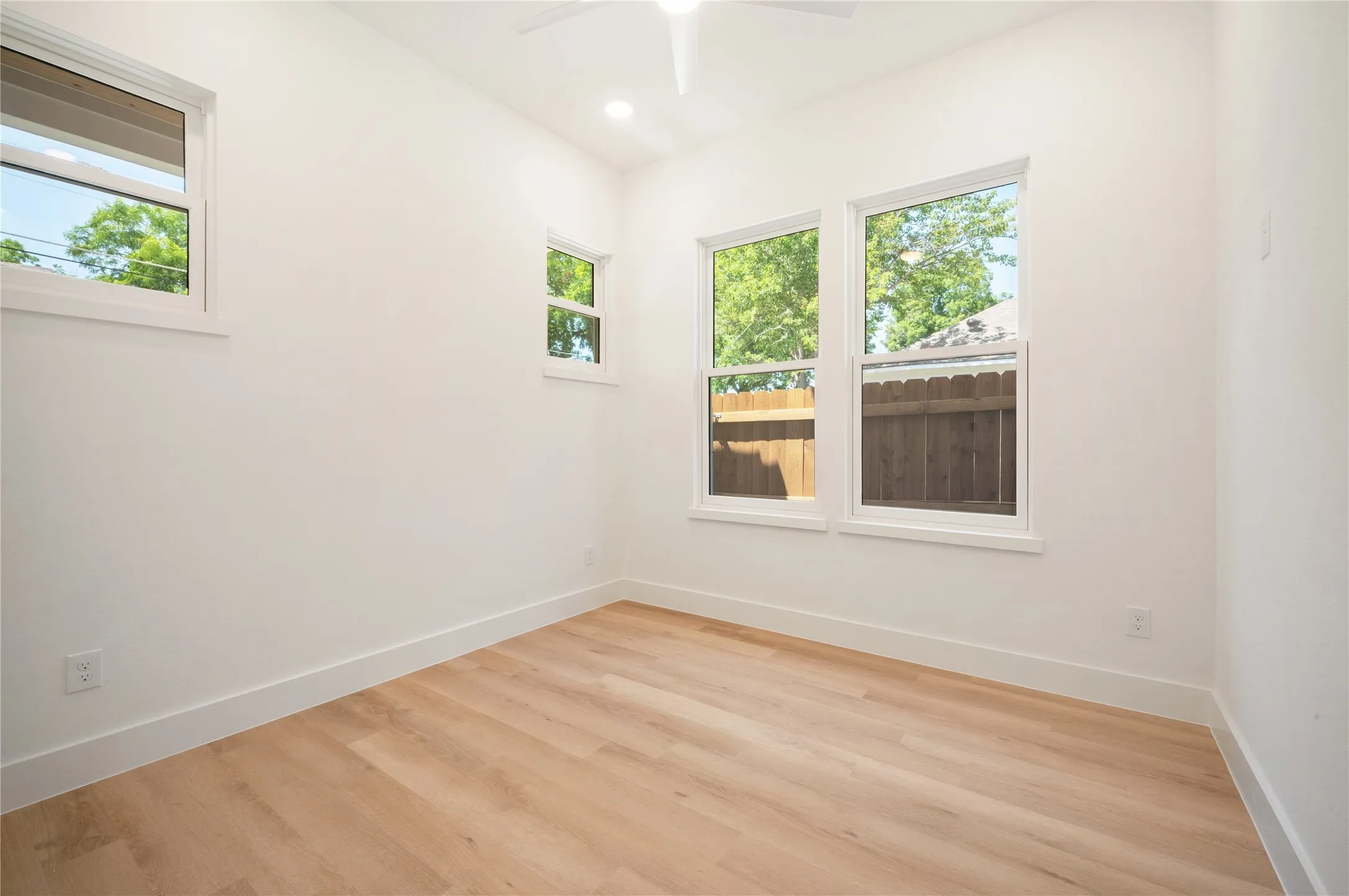 Wood-finish flooring, white walls, multiple windows, recessed lighting, and a ceiling fan