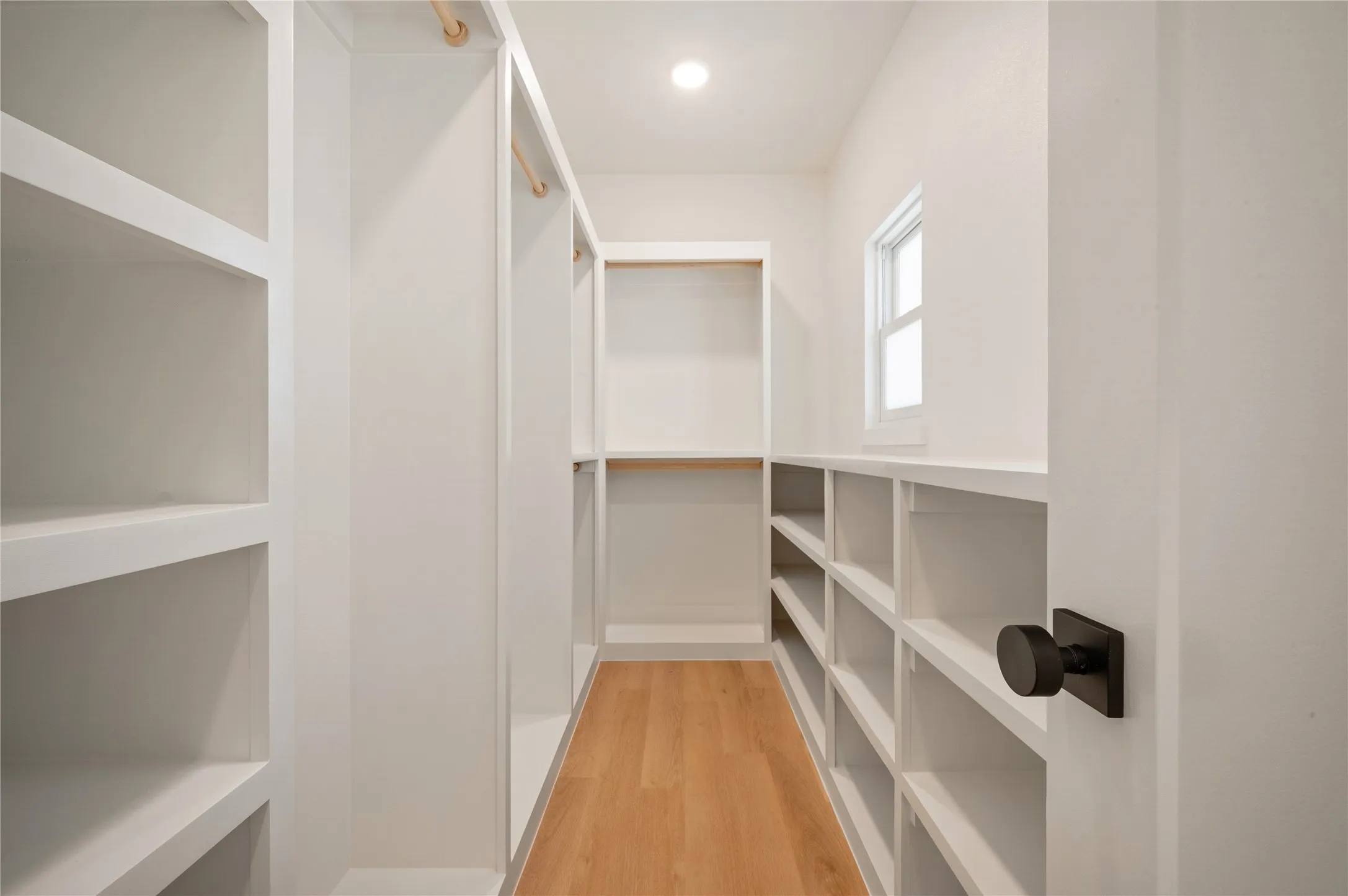 Walk-in closet featuring extensive built-in shelving, hanging rods, light wood-finish flooring, and a single window