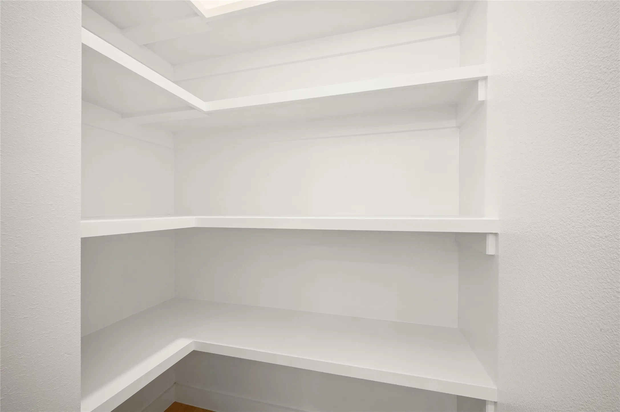 Built-in shelving with multiple levels, white finish, and corner configuration of the walk in pantry