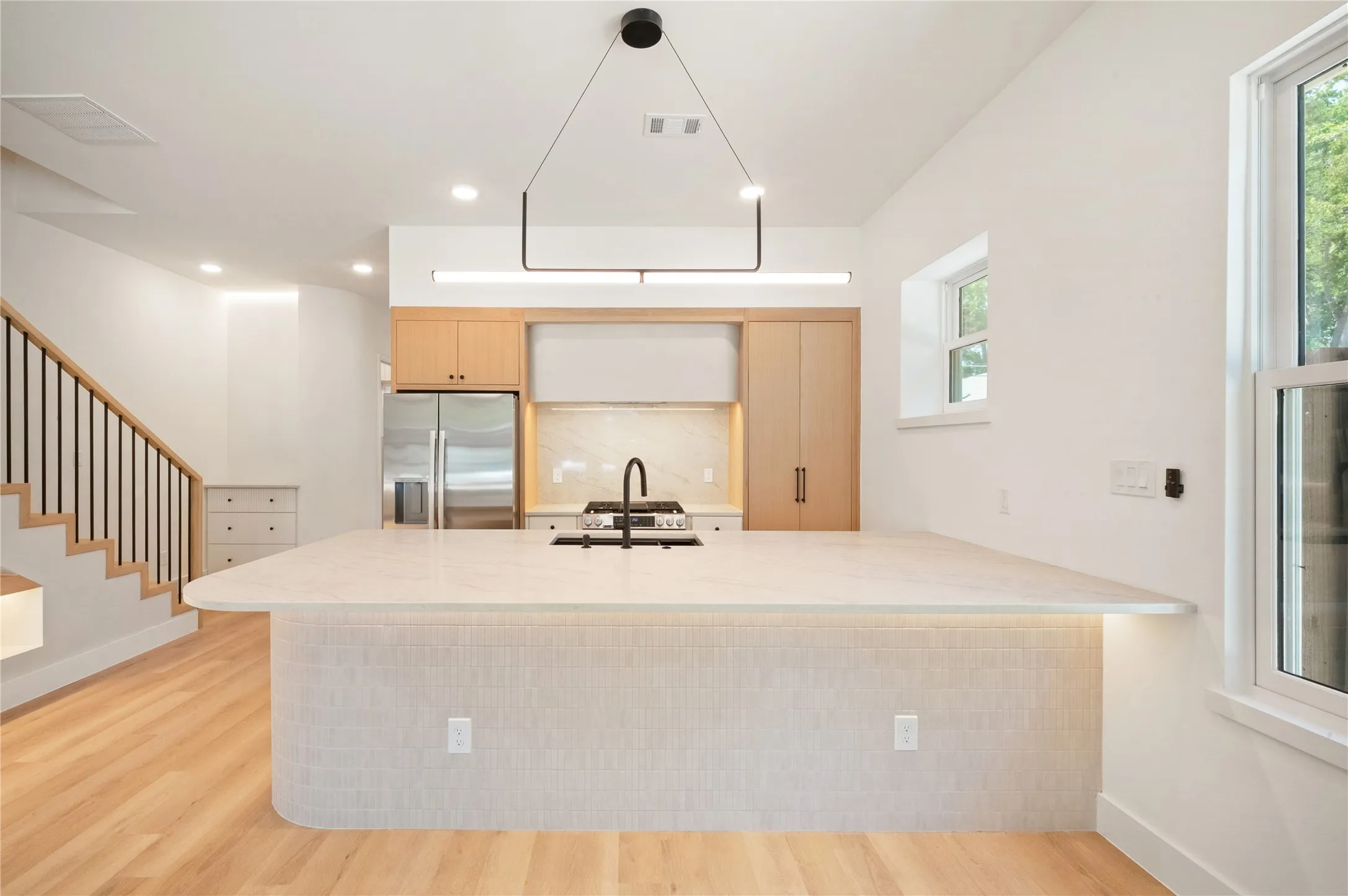 Modern kitchen featuring a large breakfast bar/island with under-cabinet lighting, light wood-finish flooring, and complementary wood cabinetry