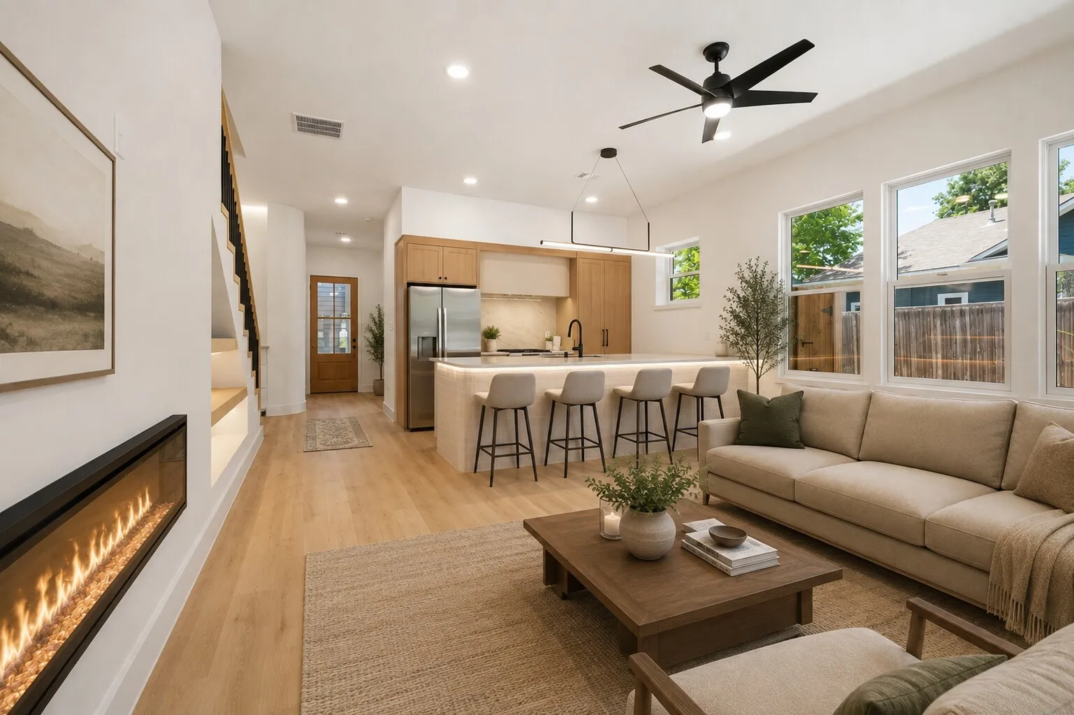 Integrated kitchen island with seating, stainless steel refrigerator, linear electric fireplace, wood-finish flooring, and a ceiling fan with integrated lighting