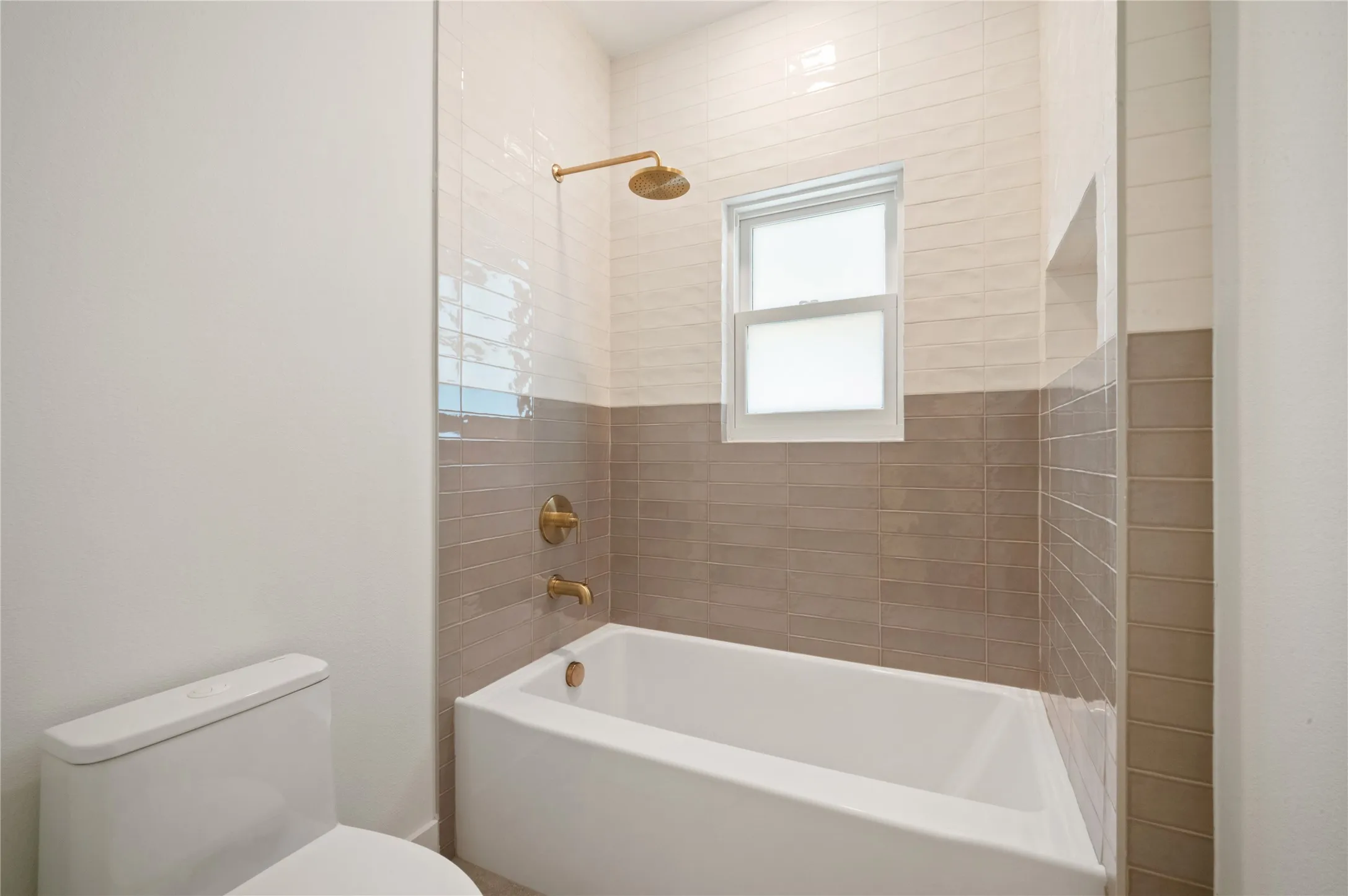 Downstairs Bathroom Bathtub with dual-tone tiled surround, integrated shower niche, and window lighting