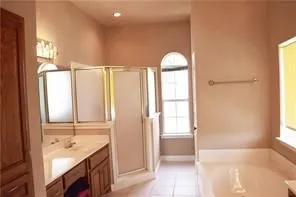 Dual vanity with integrated sinks, framed shower enclosure, arched window, and built-in tub