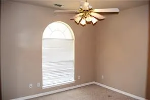 Arched window with upper transom, ceiling fan with light fixture, neutral-toned walls, and carpeted flooring