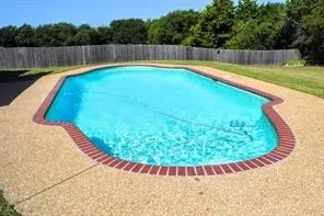In-ground swimming pool with a freeform shape, surrounded by exposed aggregate decking and a brick coping