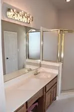 Dual vanity with integrated sinks and wood-finish cabinetry, illuminated by a decorative light fixture