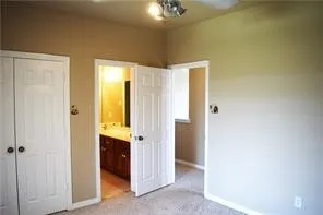 Carpeted flooring, ceiling fan with integrated lighting, paneled doors, and a bathroom with a vanity, mirror, and overhead lighting