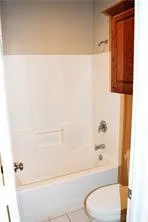 White bathtub with integrated shower, chrome fixtures, and a wall-mounted wooden cabinet