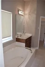 Built-in soaking tub, single vanity with wood-finish cabinetry, countertop with integrated sink, wall-mounted mirror, and decorative light fixture