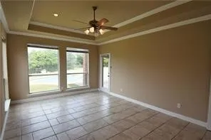 Recessed ceiling with crown molding, ceiling fan with integrated lighting, tiled flooring, and multiple windows