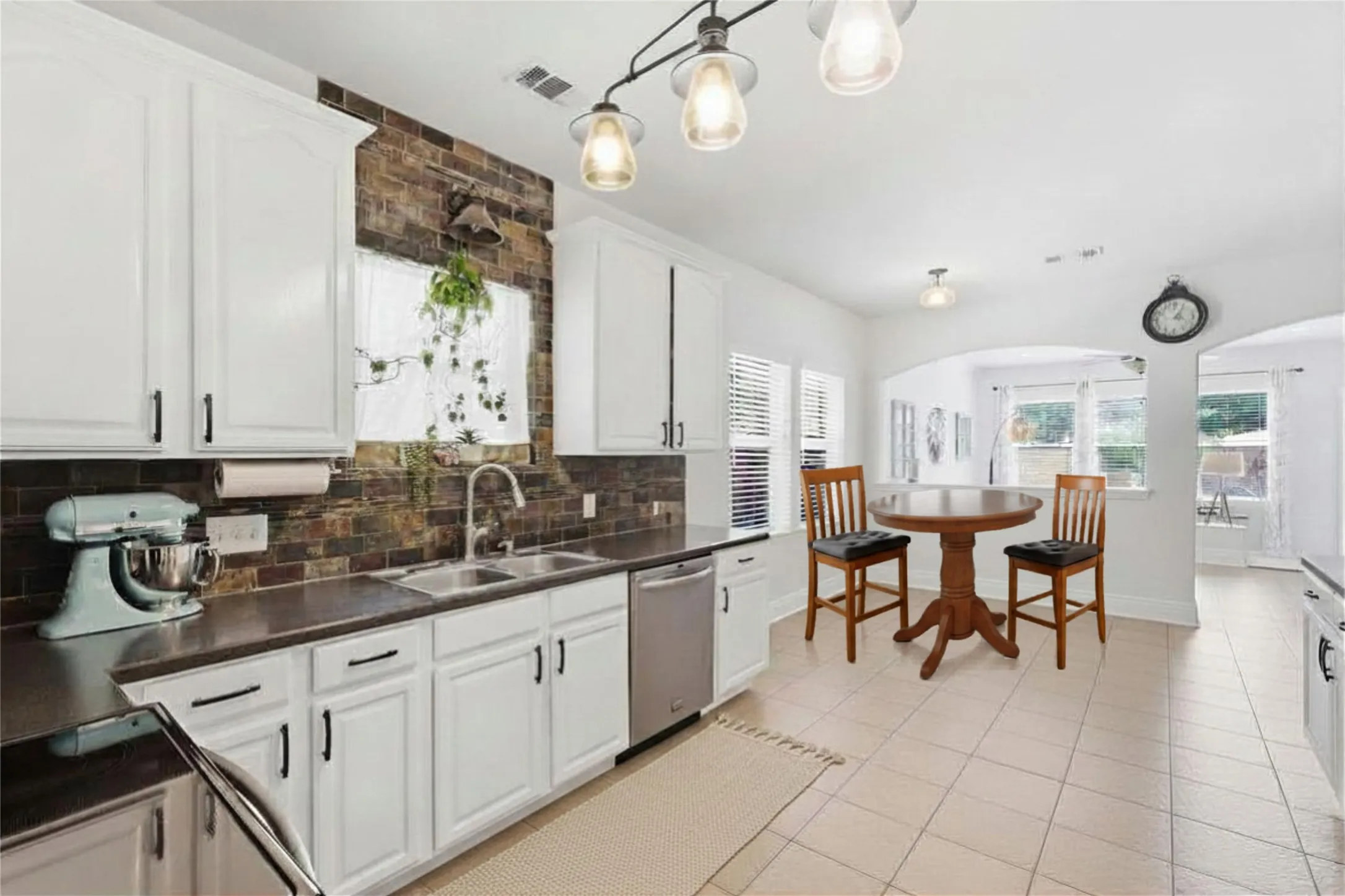 Bright kitchen featuring white cabinetry, dark countertops, a tile backsplash, stainless steel appliances, and tile flooring