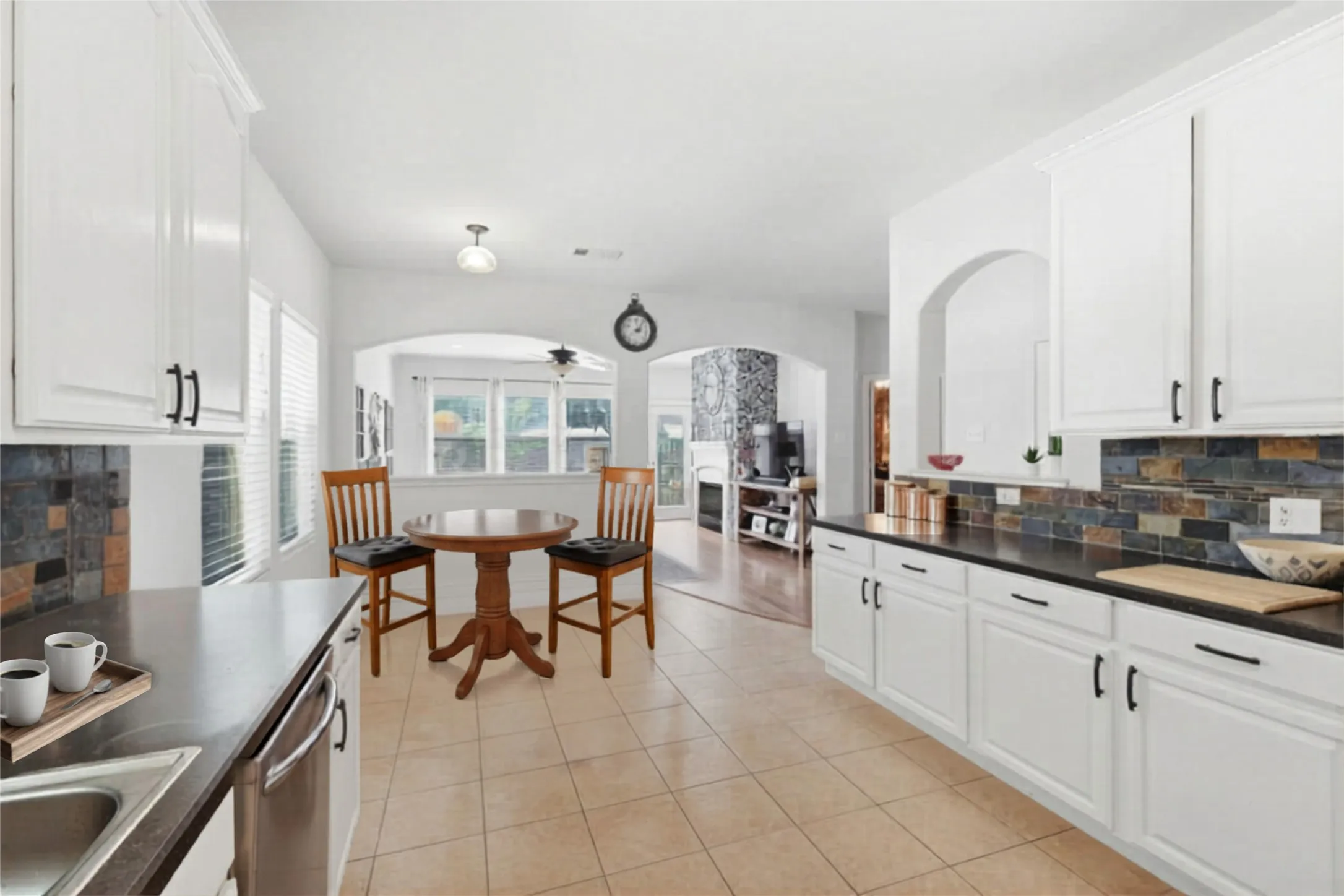 Kitchen featuring white cabinetry with dark hardware, dark countertops, and a multi-toned tile backsplash