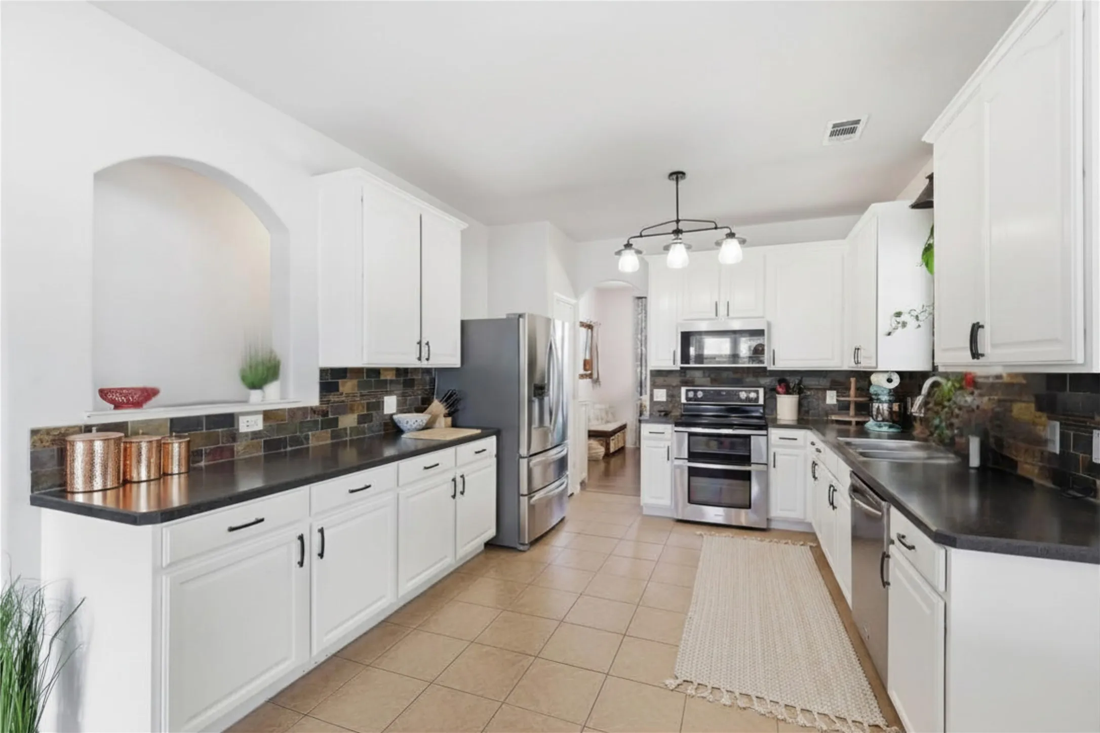 Kitchen featuring white cabinetry, dark countertops, a tiled backsplash, stainless steel appliances, and tile flooring