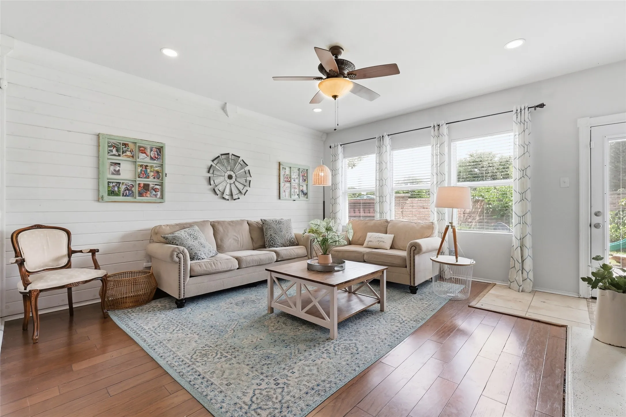 Spacious living area featuring wood-finish flooring, white shiplap accent wall, recessed lighting, and a ceiling fan