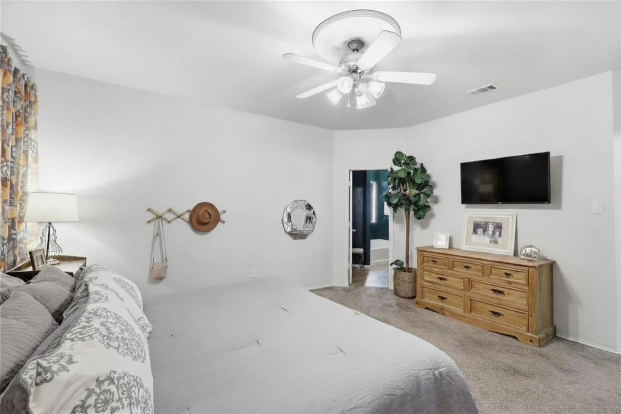 Carpeted room with a ceiling fan, light gray walls, and a wall-mounted flat-screen television