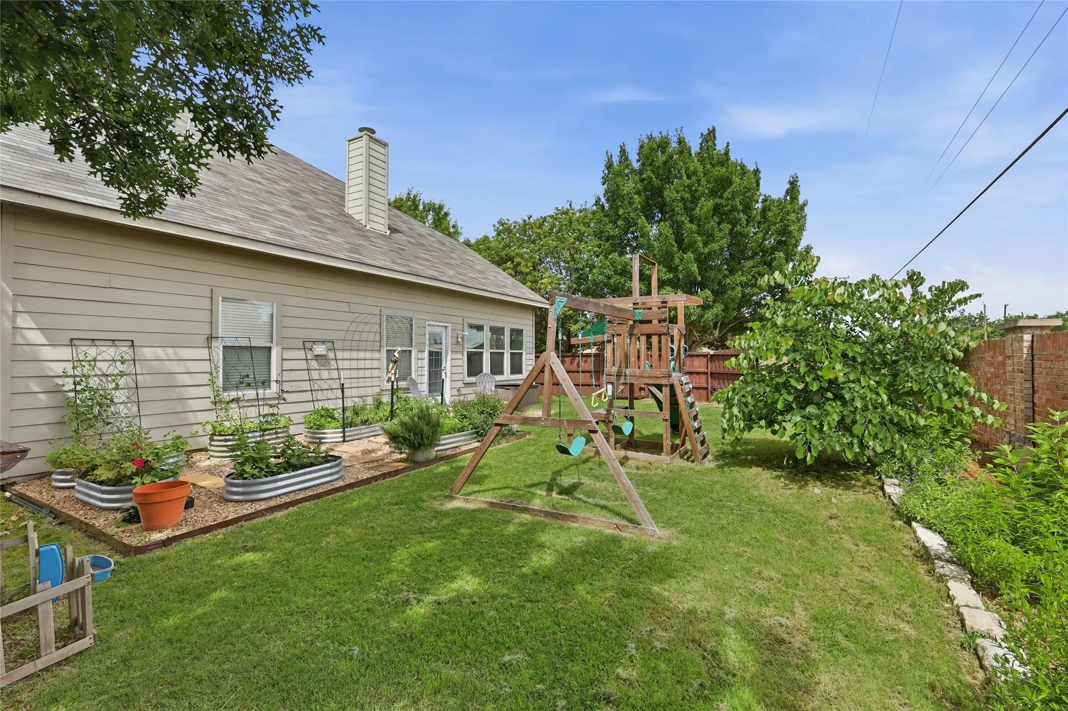 Spacious backyard featuring a manicured lawn, an established garden area with raised beds, and mature trees