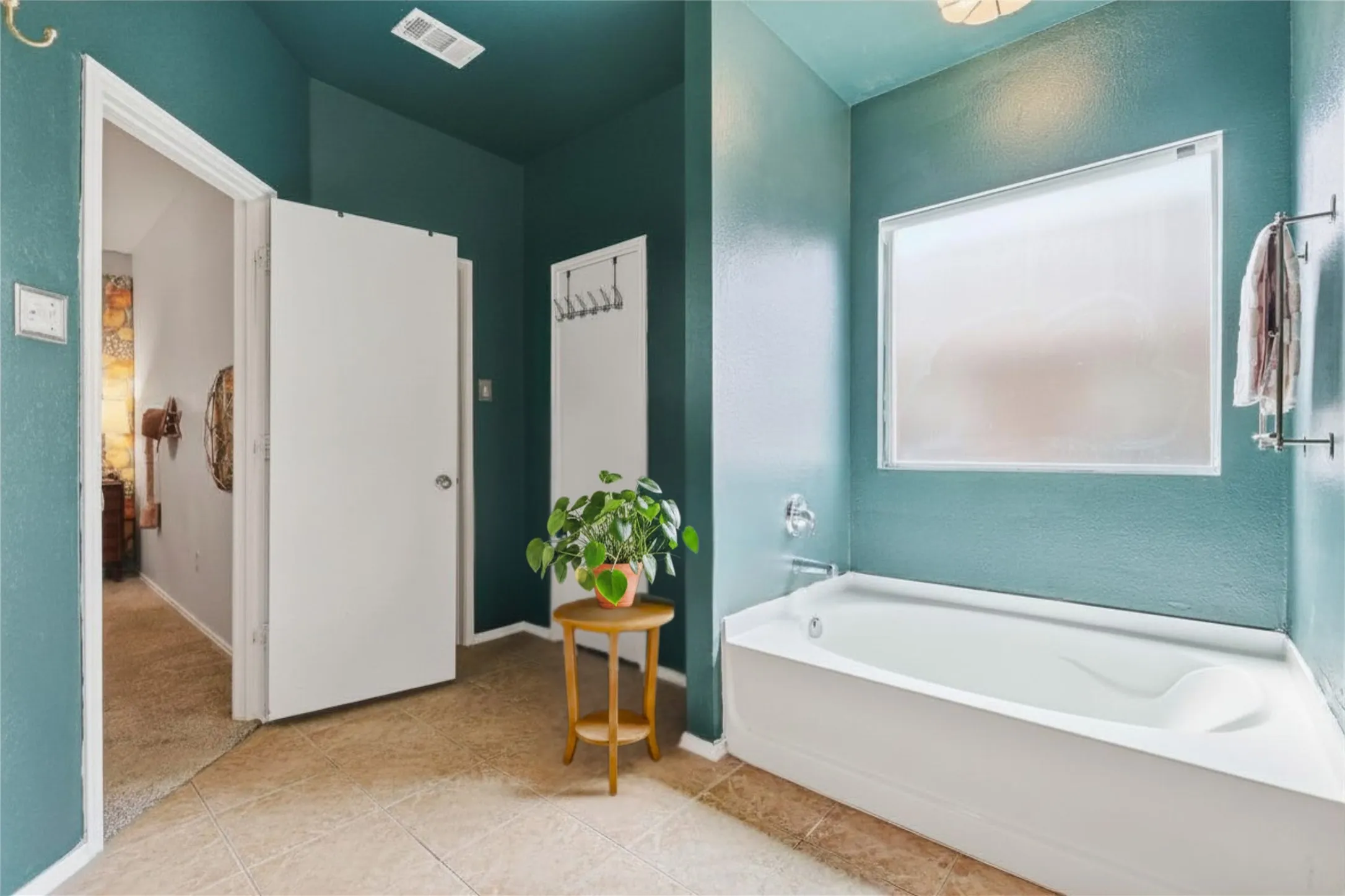 Soaking tub with chrome fixtures, frosted window, and tiled flooring