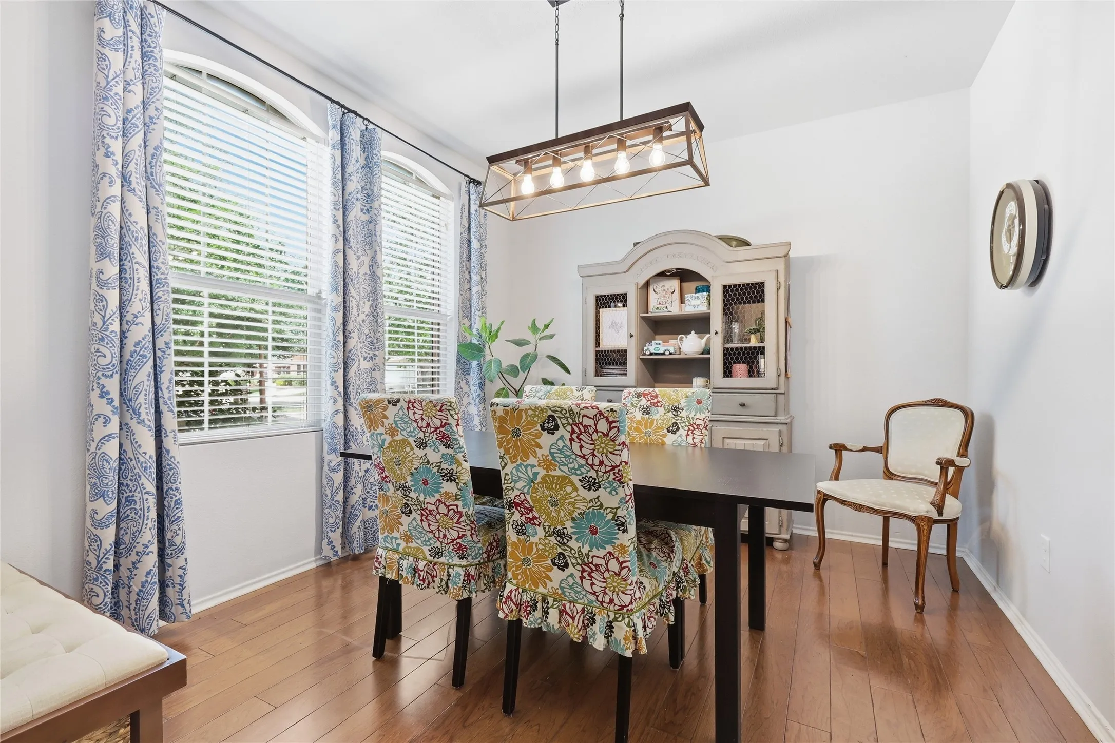 Well-lit dining area featuring wood-finish flooring, two arched windows with blinds, and a linear chandelier