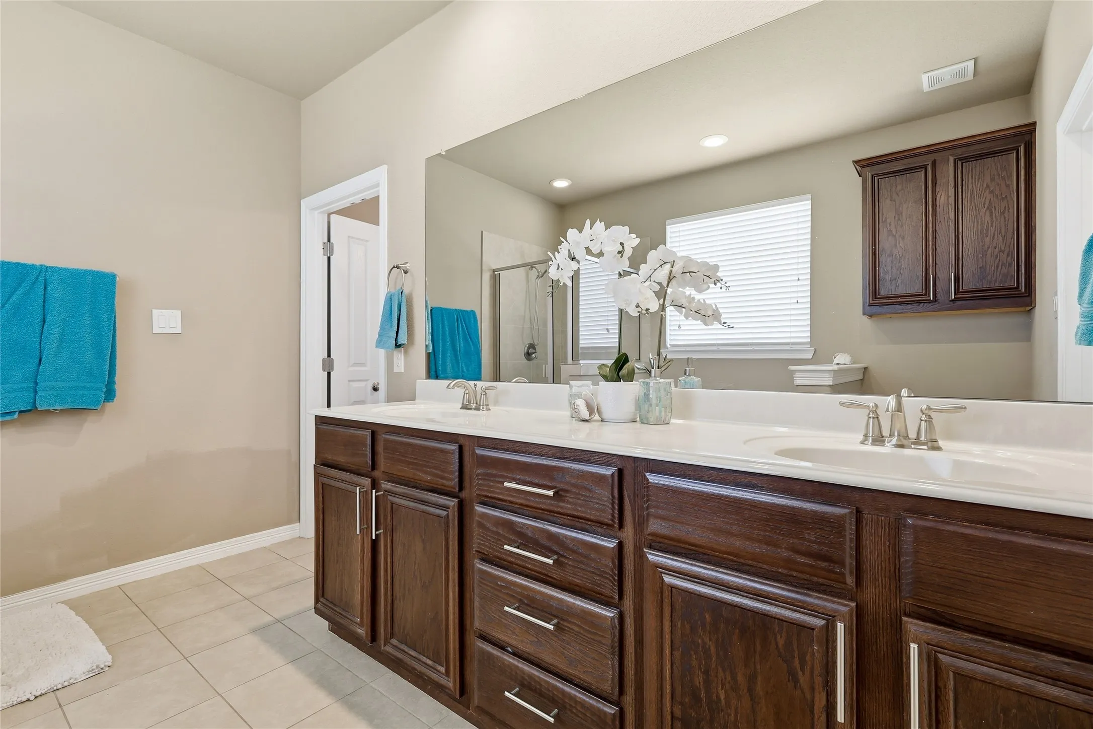 Bathroom vanity featuring dual sinks with integrated white countertops, dark wood-finish cabinetry, and chrome fixtures