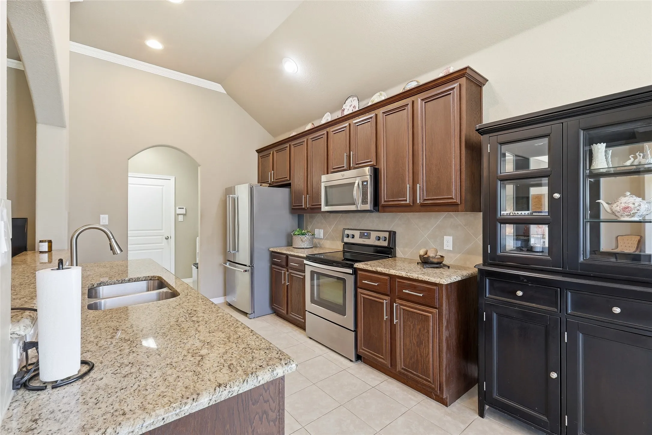 Kitchen featuring vaulted ceilings, granite countertops, wood-finish cabinetry, stainless steel appliances, and tile flooring