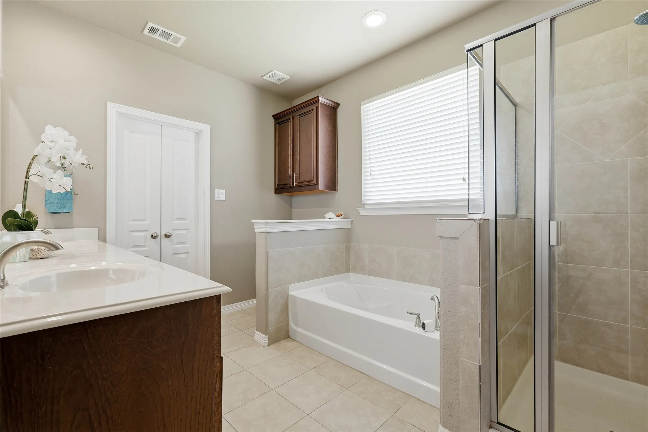 Bathroom featuring a dual vanity with undermount sinks, a soaking tub, a separate glass-enclosed shower, and tile flooring